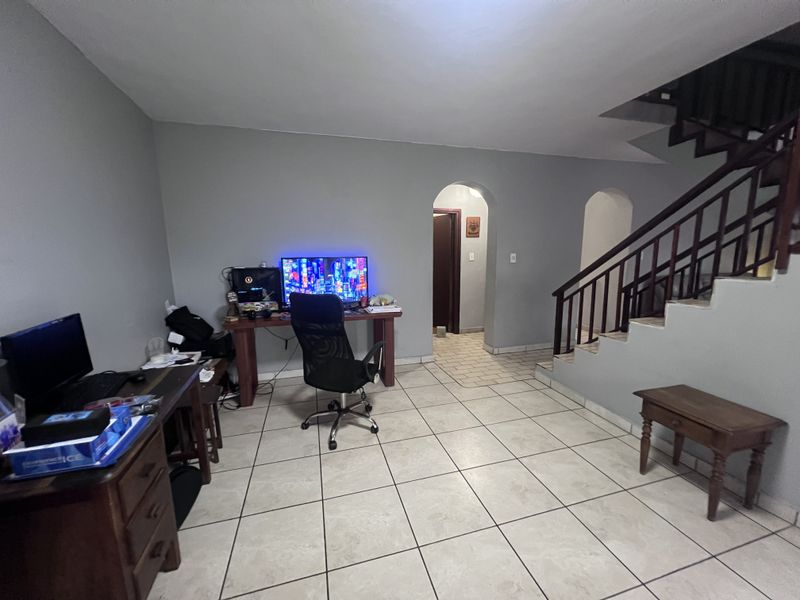 Open-plan living area featuring tiled flooring, a wooden staircase with balustrade, and arched doorways leading to other sections of the townhouse.