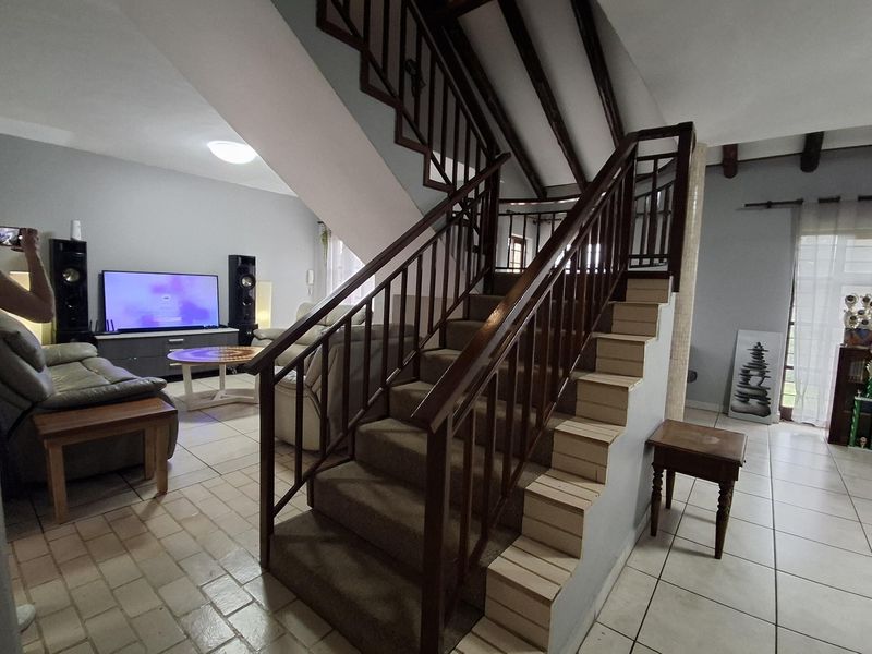 Open plan living area featuring a central staircase with wooden balustrades, exposed ceiling beams, and tiled flooring throughout.