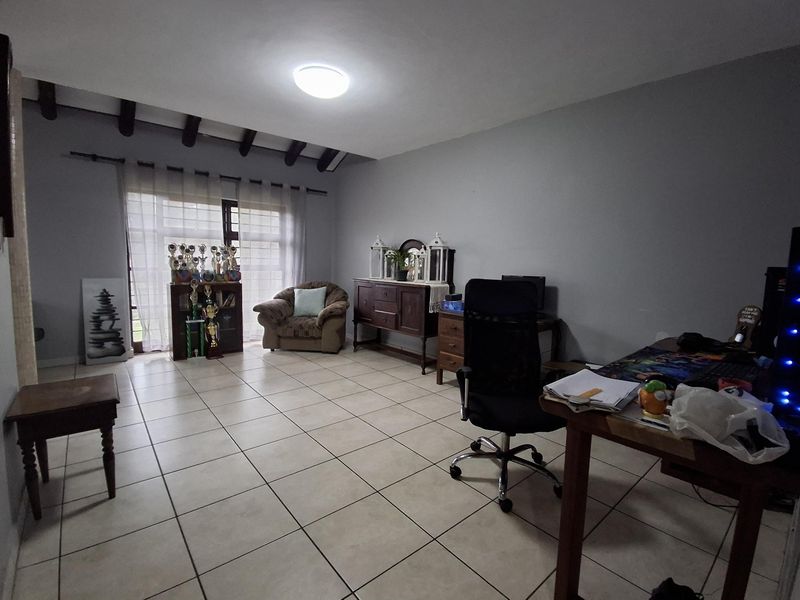 Spacious living area featuring tiled flooring, exposed ceiling beams, and a sliding glass door providing natural light and access to the exterior.