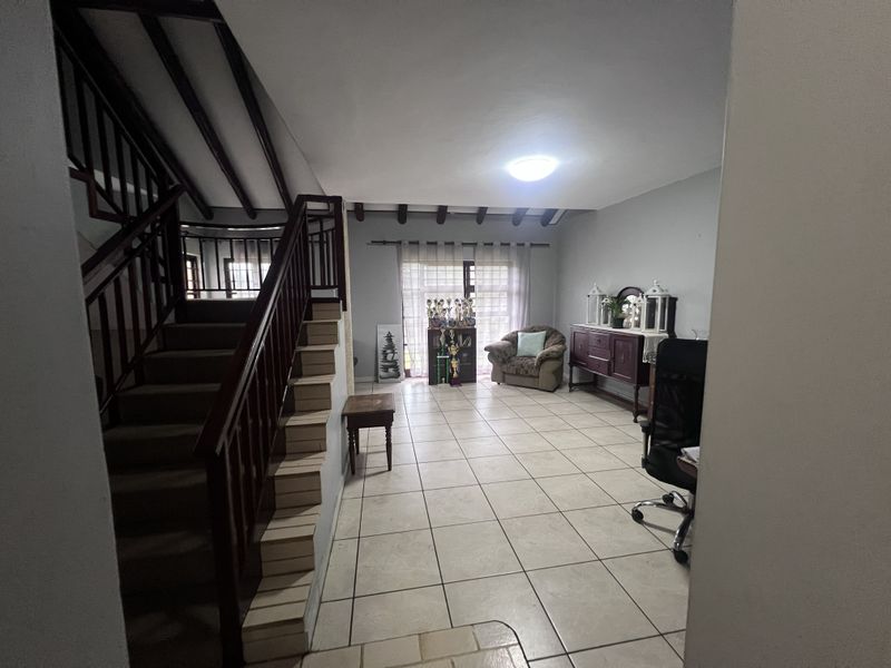 Spacious living area featuring tiled flooring, exposed ceiling beams, and a wooden staircase with a matching balustrade leading to the upper level.