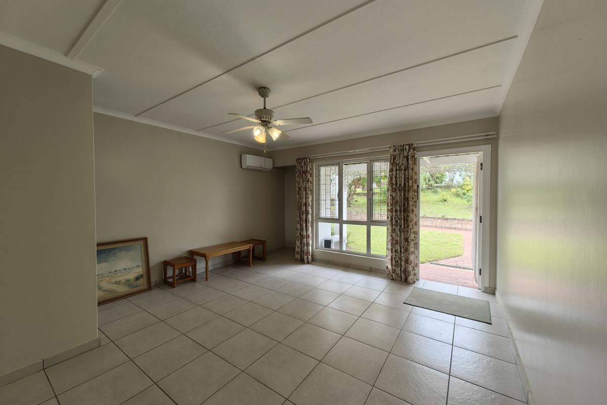 A bright living room featuring tiled flooring, a ceiling fan, and a wall-mounted air conditioning unit, with direct access to a rear garden patio.