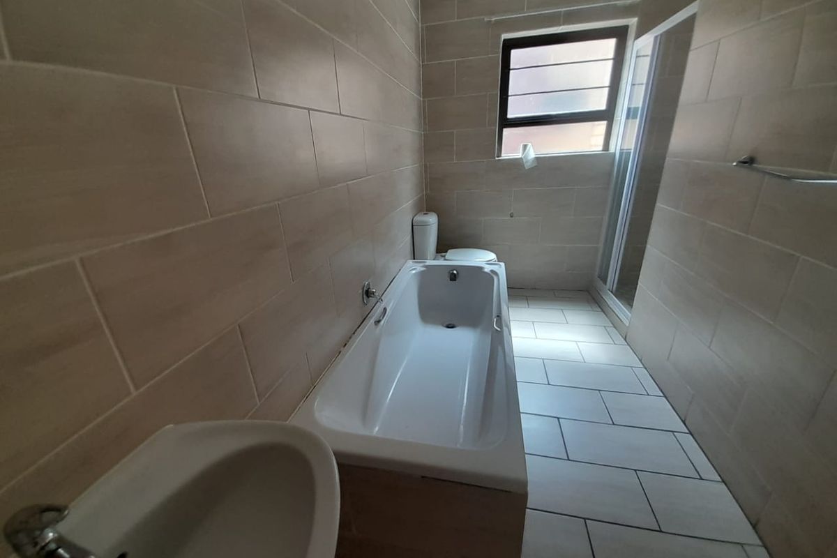 A modern bathroom featuring floor-to-ceiling neutral tiling, a built-in bathtub, a separate shower enclosure, and a standard toilet.