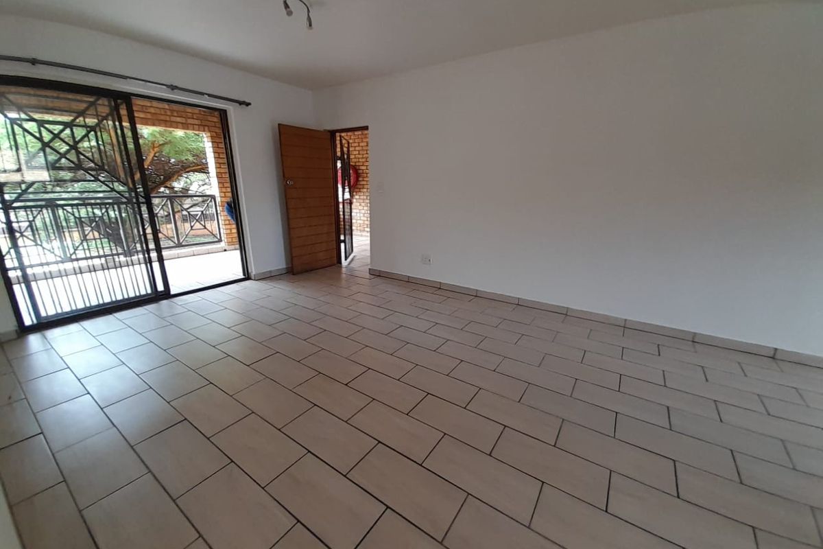 An empty living room featuring neutral floor tiles, a sliding glass door leading to a patio, and a wooden door providing access to the exterior.