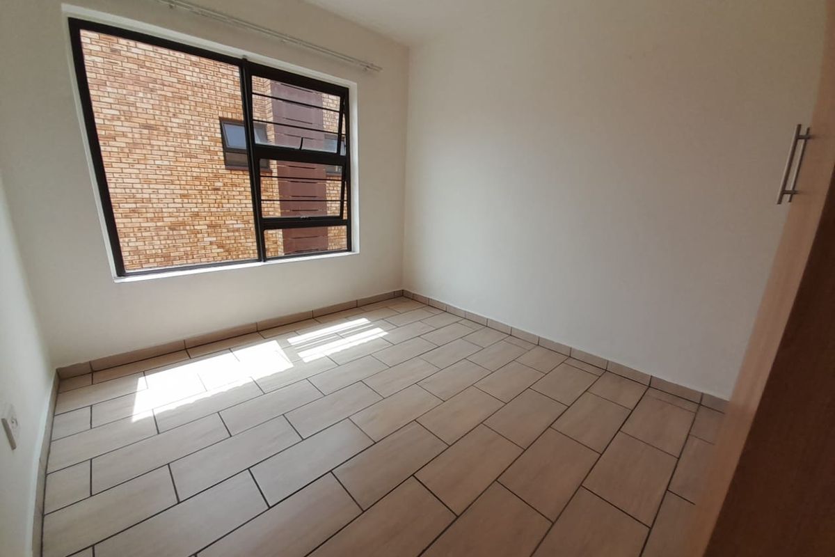 A bright, empty bedroom featuring neutral floor tiles, a large window, and built-in cupboard storage.