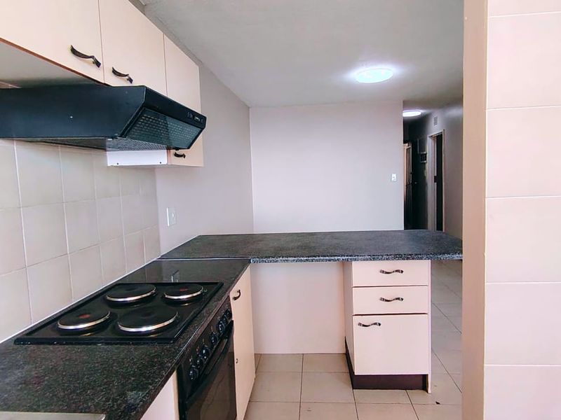 A functional kitchen featuring built-in cabinetry, dark countertops, an electric hob, oven, and extractor fan, with neutral tiled flooring and backsplash.