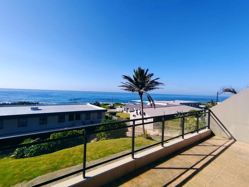 A spacious balcony featuring tiled flooring and a metal balustrade, offering expansive views of the ocean and surrounding coastal landscape.