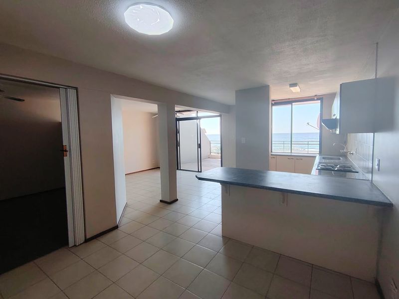 Open plan living and kitchen area featuring tiled floors, a breakfast bar, and direct access to a balcony with ocean views.