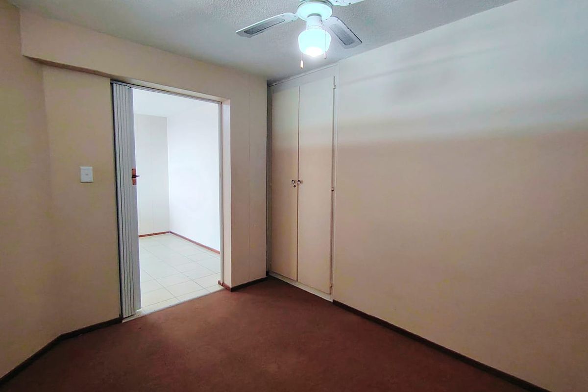 An empty bedroom featuring a built-in wardrobe, ceiling fan, and a folding door leading to an adjacent tiled space.