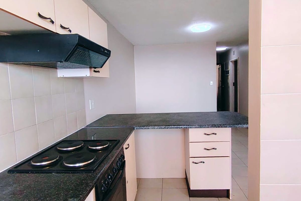 A functional kitchen featuring built-in cabinetry, dark countertops, an electric hob, oven, and extractor fan, with neutral tiled flooring and backsplash.