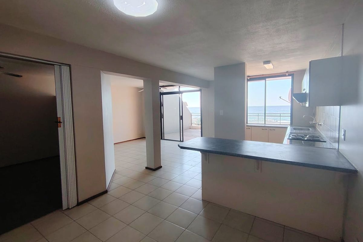 Open plan living and kitchen area featuring tiled floors, a breakfast bar, and direct access to a balcony with ocean views.