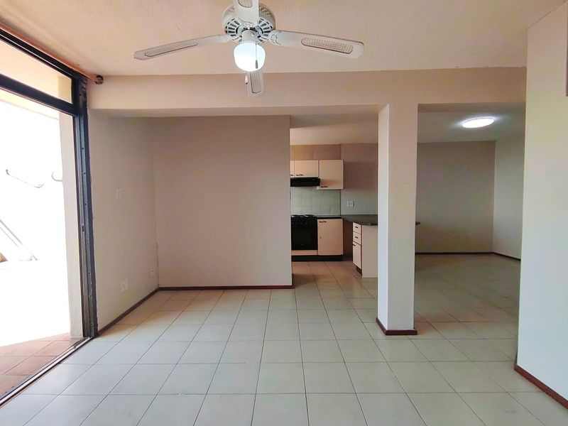An open-plan living and kitchen area featuring tiled flooring, a ceiling fan, and built-in kitchen cabinetry with an integrated oven and extractor fan.