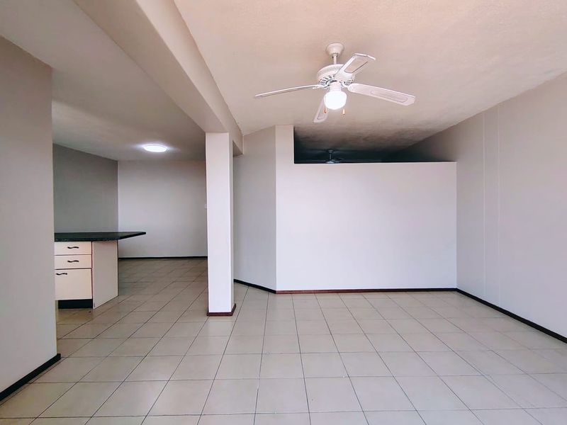An open-plan living and kitchen area featuring tiled flooring, a central structural column, and a ceiling fan, offering a blank canvas for customization.