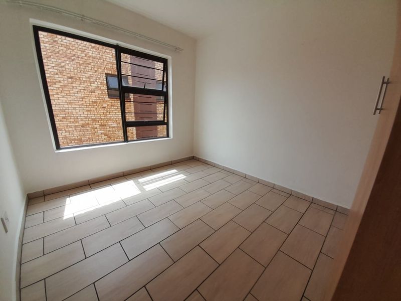 A bright, empty bedroom featuring neutral floor tiles, a large window, and built-in cupboard storage.