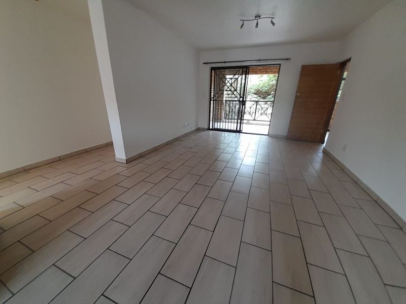 An open-plan living area featuring neutral floor tiles, a ceiling-mounted light fixture, and a sliding door providing access to an outdoor patio.