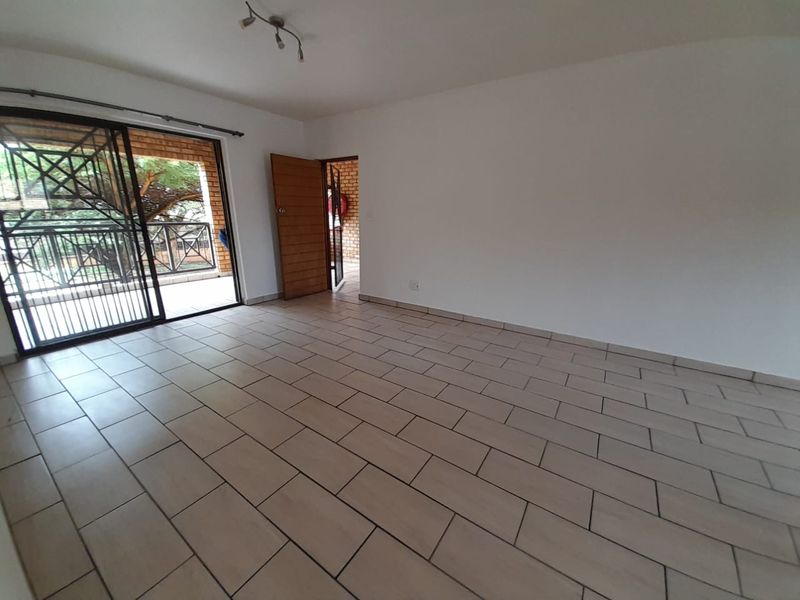 An empty living room featuring neutral floor tiles, a sliding glass door leading to a patio, and a wooden door providing access to the exterior.