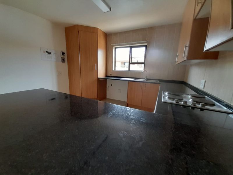 Functional kitchen featuring dark granite countertops, light wood cabinetry, a built-in electric hob, and a stainless steel sink.