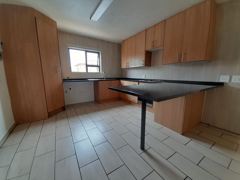 A functional kitchen featuring light wood cabinetry, dark granite countertops, a breakfast bar, and tiled flooring.