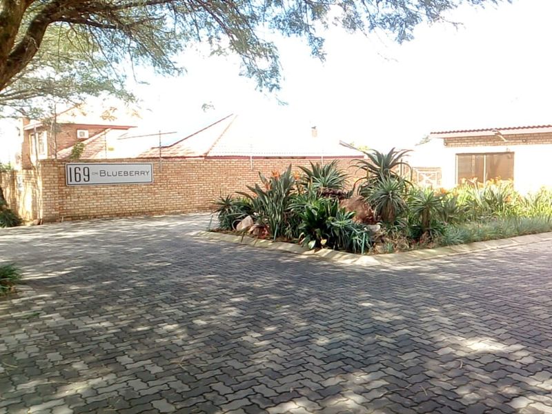 A view of the townhouse complex entrance featuring paved driveway, brick boundary wall, and landscaped garden beds.
