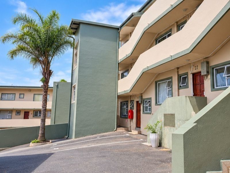 Exterior view of an apartment complex featuring a paved driveway, external staircases, and painted building facade.