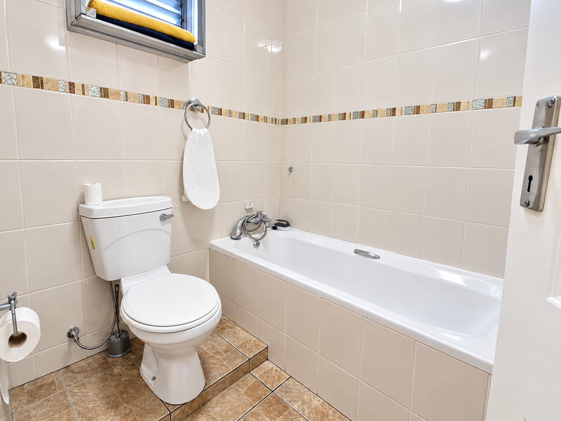 A functional bathroom featuring a standard bathtub, toilet, and neutral wall tiling with a decorative mosaic border.