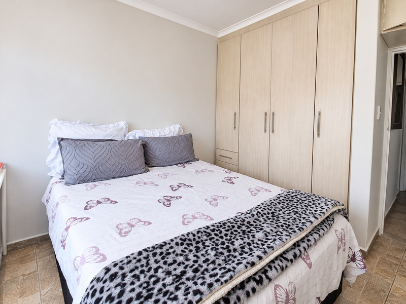 A well-maintained bedroom featuring light wood-finish built-in wardrobes and neutral tiled flooring, offering a clean and functional living space.