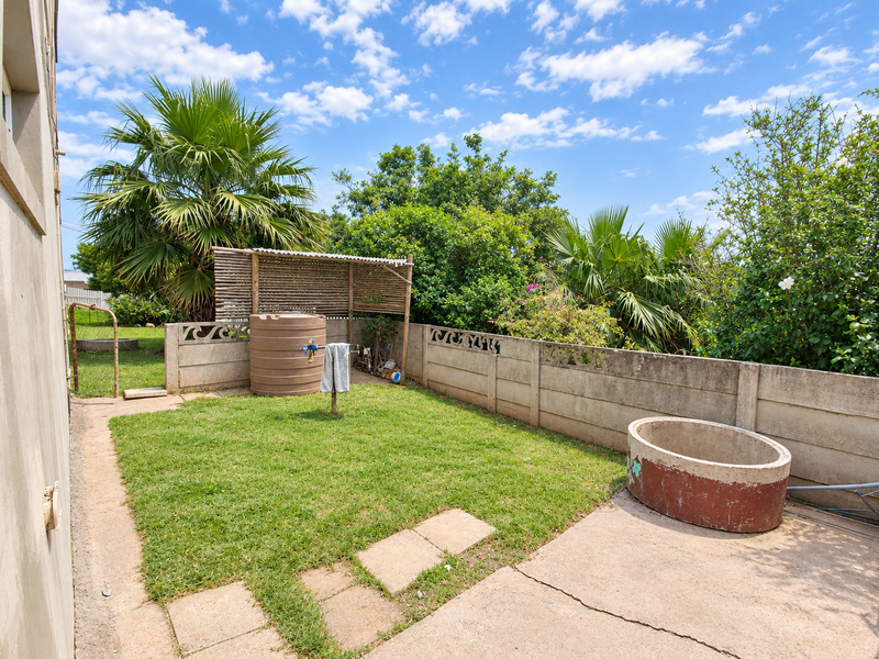 A private rear garden featuring a lawn, concrete patio area, boundary wall, and water storage tank, offering potential for outdoor landscaping improvements.