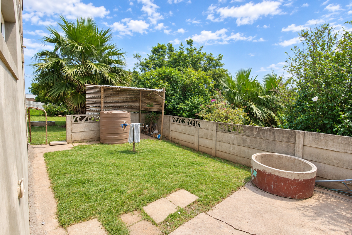 A private rear garden featuring a lawn, concrete patio area, boundary wall, and water storage tank, offering potential for outdoor landscaping improvements.