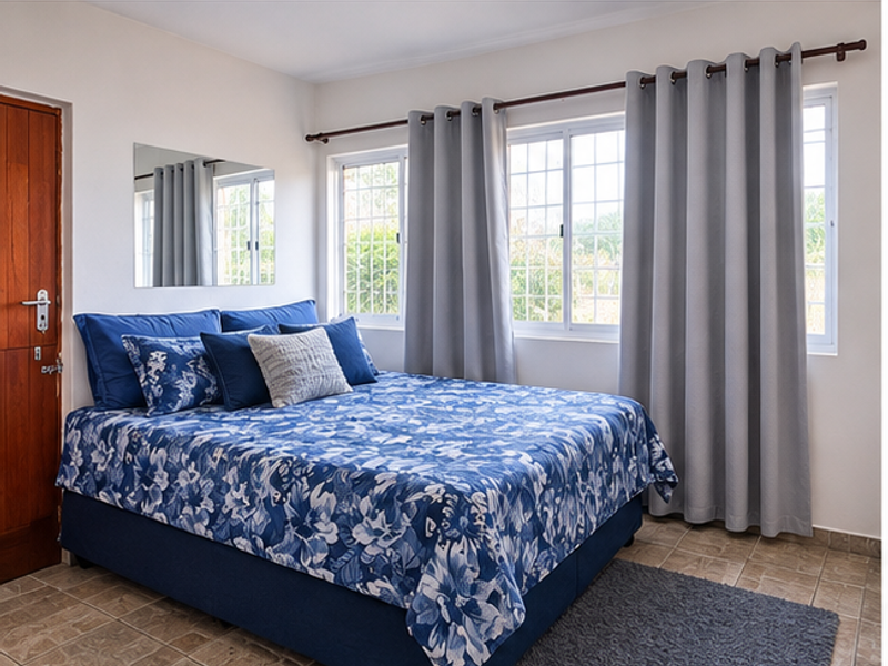 A well-lit bedroom featuring tiled flooring, a wooden door, and large windows with security bars, providing a comfortable and functional living space.