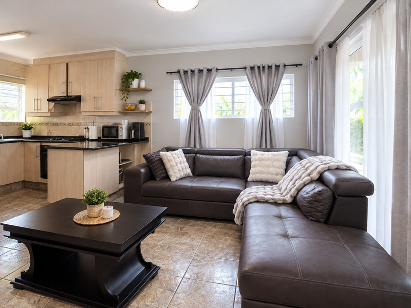 Open-plan living area featuring a functional kitchen with built-in cabinetry, granite countertops, and tiled flooring, seamlessly connected to a comfortable lounge space.