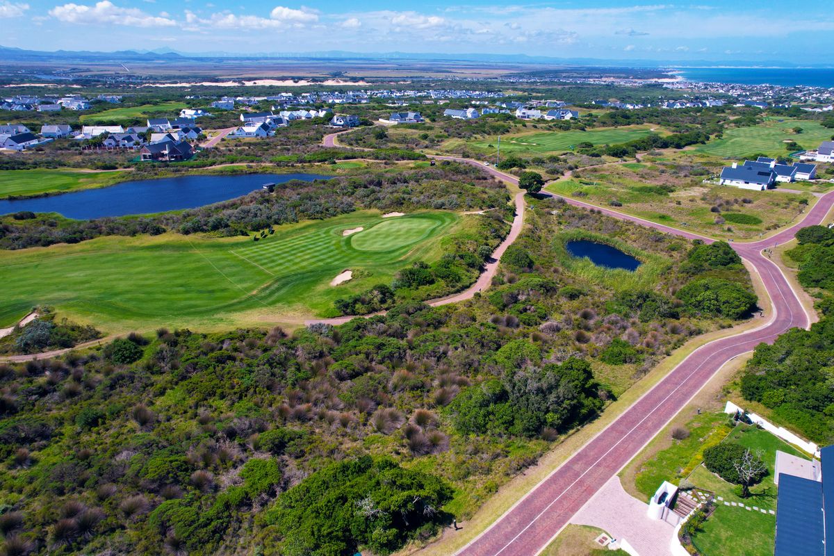 An aerial view of a residential estate featuring a golf course, natural landscape, and paved road infrastructure.