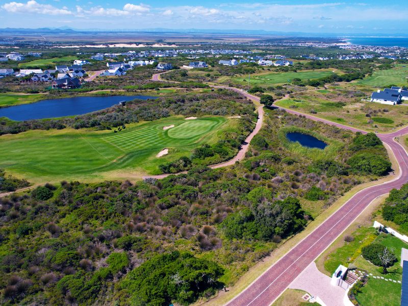 An aerial view of a residential estate featuring a golf course, natural landscape, and paved road infrastructure.