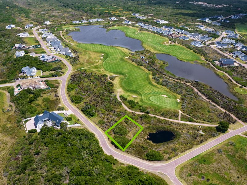 Aerial view of a vacant residential plot situated within a golf estate, featuring paved road access and proximity to natural landscape and water features.