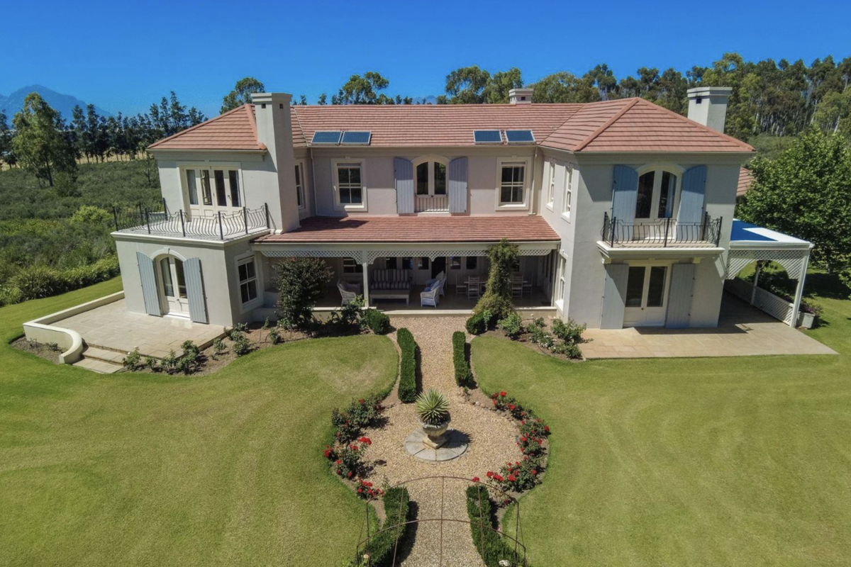 Aerial view of a grand farmhouse featuring a terracotta tiled roof, solar panels, covered patio, and beautifully landscaped gardens with manicured pathways.