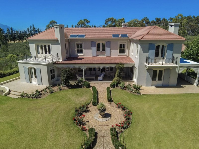 Aerial view of a grand farmhouse featuring a terracotta tiled roof, solar panels, covered patio, and beautifully landscaped gardens with manicured pathways.