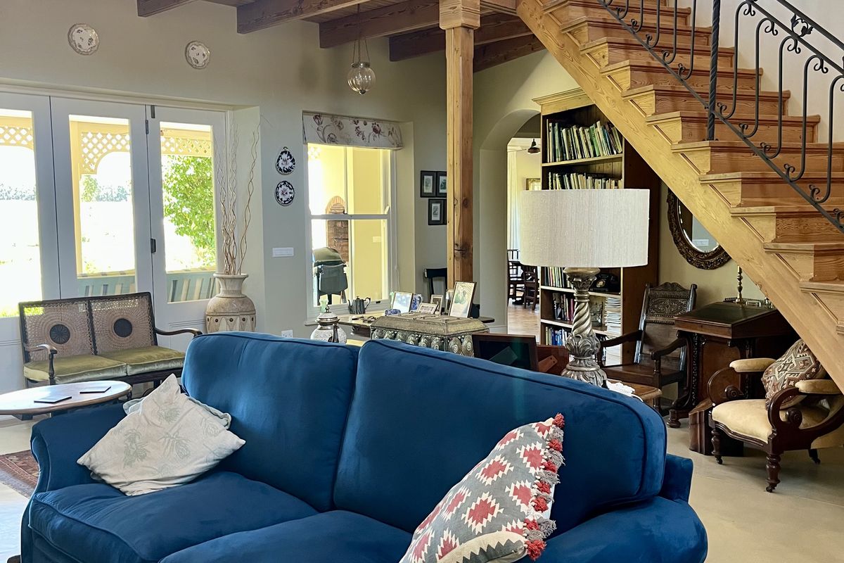 Spacious living room featuring a double-volume ceiling with exposed wooden beams, a grand wooden staircase with wrought iron railings, and polished concrete floors.