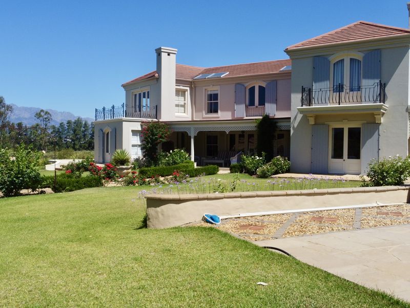 A well-maintained rear elevation of a farm-style residence featuring a swimming pool, landscaped garden, covered patio, and upper-level balconies with mountain views.