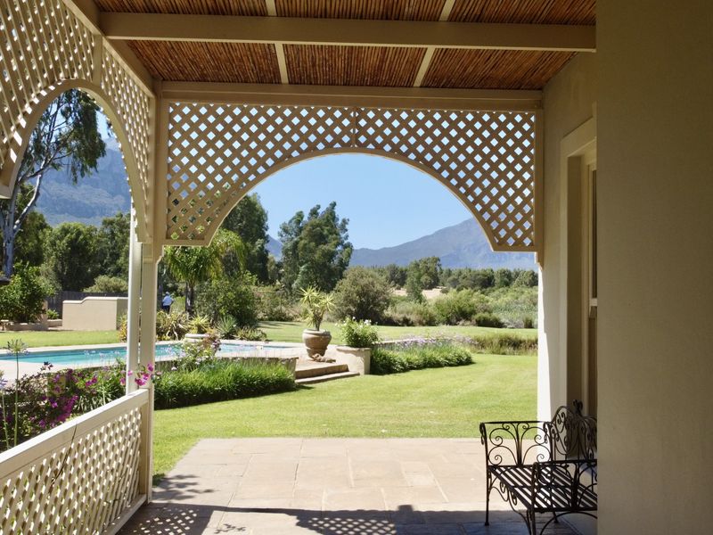 A covered patio featuring timber lattice detailing and a bamboo ceiling, overlooking a well-maintained garden and swimming pool with mountain views.