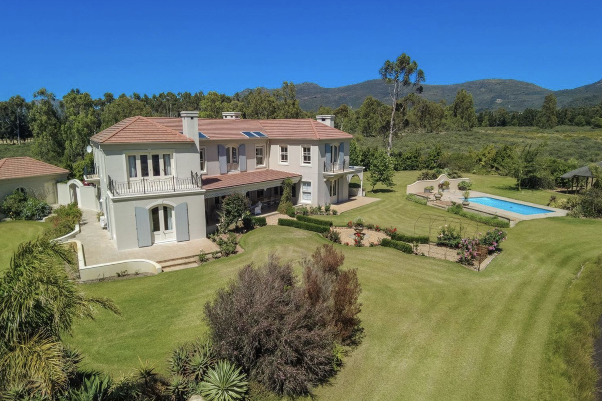 Aerial view of a large farm estate featuring a well-maintained residence, expansive lawns, landscaped gardens, and a private swimming pool set against a mountain backdrop.