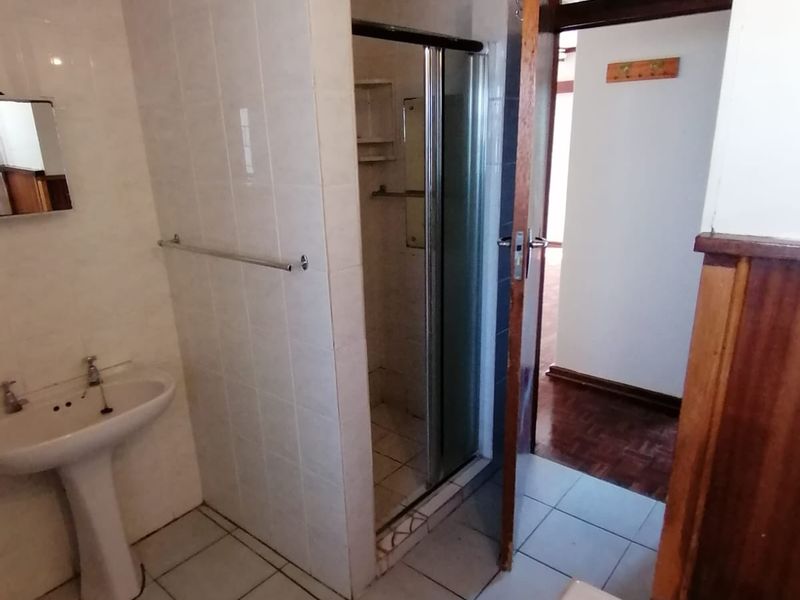 A dated bathroom featuring a pedestal basin, shower enclosure, and bathtub with exposed timber ceiling beams and tiled finishes.