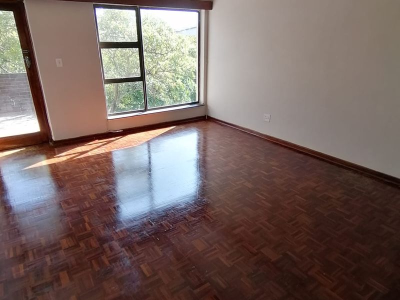 Spacious living area featuring polished parquet flooring, exposed timber ceiling beams, a ceiling fan, and direct access to an outdoor balcony through a glass door.
