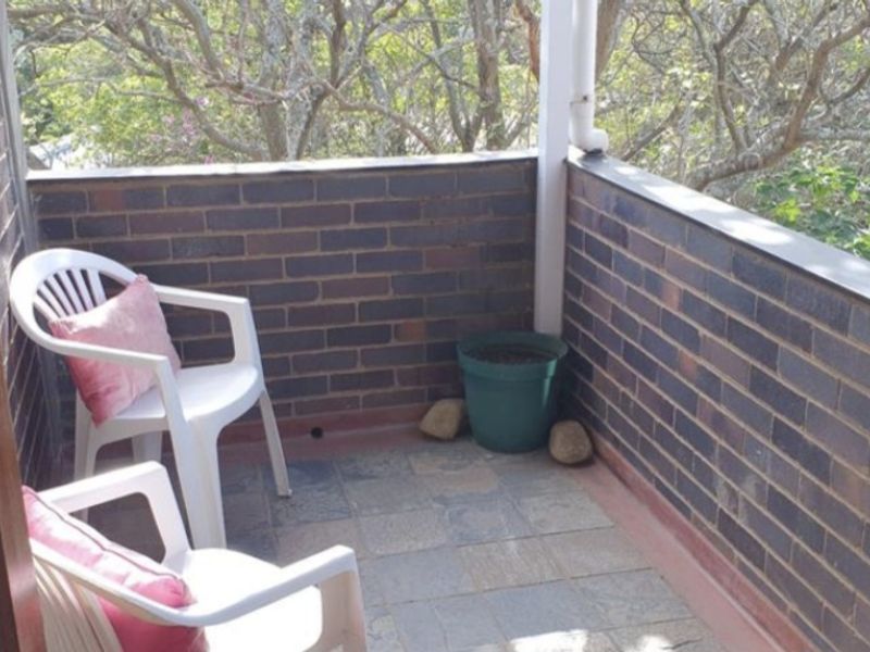 A compact balcony featuring brick walls and tiled flooring, offering a private outdoor space with a view of surrounding trees.