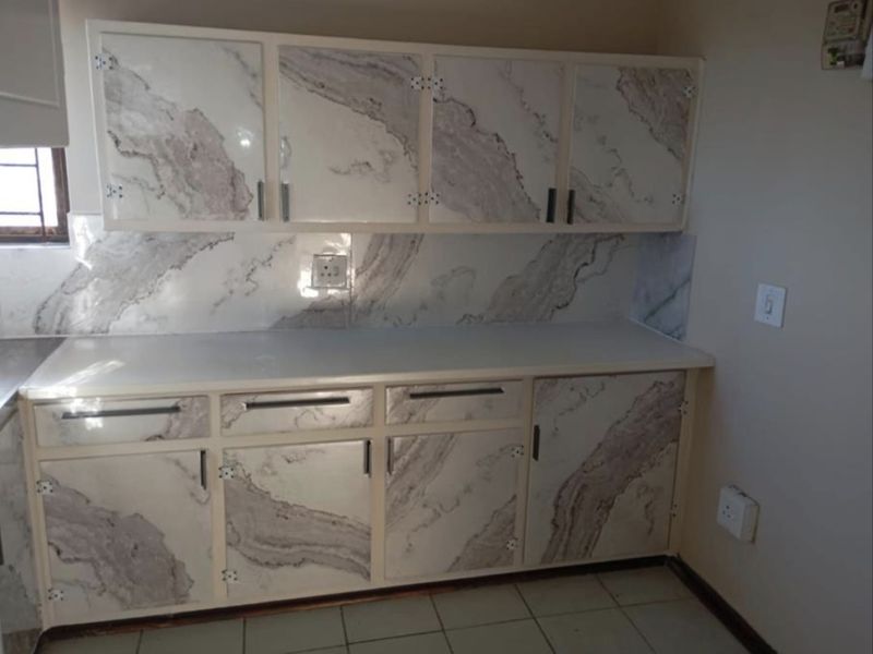 A compact kitchen area featuring built-in cabinetry with a marble-effect finish, tiled backsplash, and tiled flooring, offering a functional space for culinary activities.