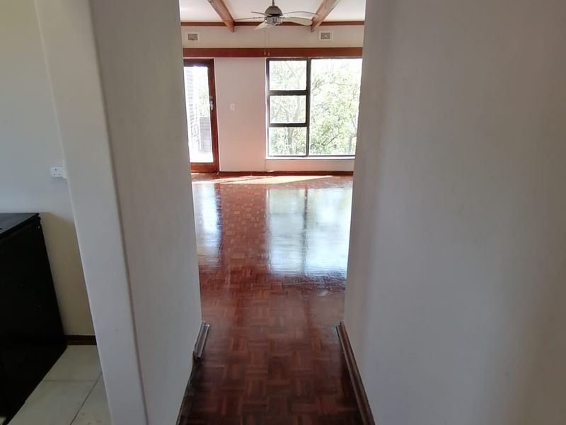 A bright hallway featuring polished parquet flooring and exposed timber ceiling beams, leading into an open-plan living area with large windows.