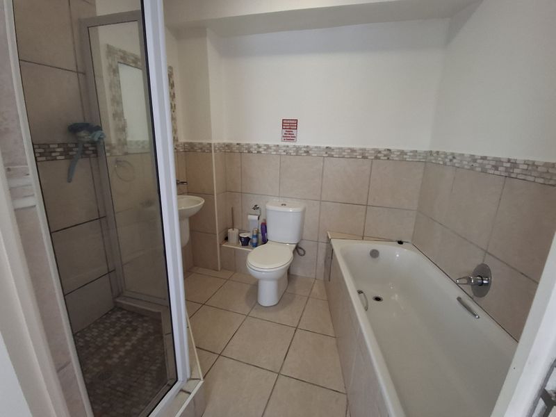 A functional bathroom featuring a separate shower enclosure, bathtub, pedestal basin, and toilet with neutral wall and floor tiling.