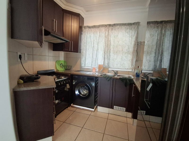A functional kitchen featuring dark wood cabinetry, tiled flooring, a built-in oven with extractor fan, and a stainless steel sink.