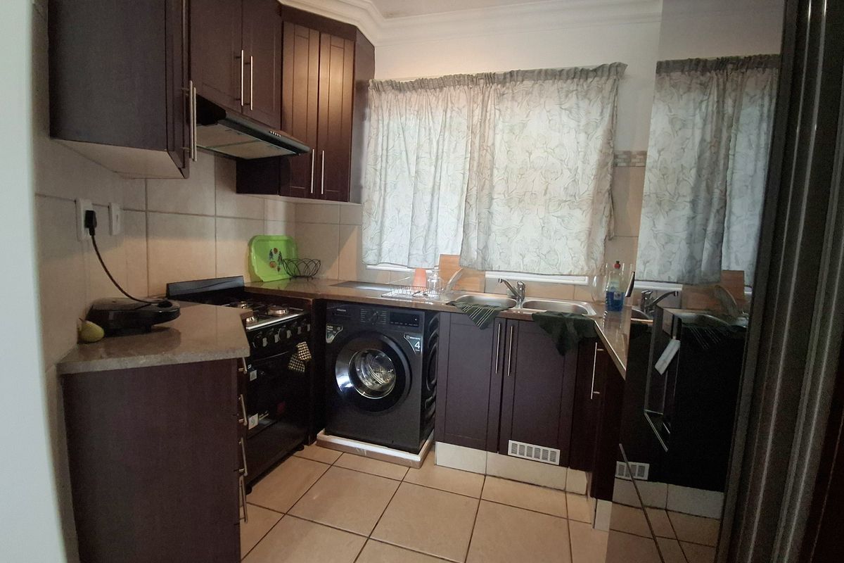 A functional kitchen featuring dark wood cabinetry, tiled flooring, a built-in oven with extractor fan, and a stainless steel sink.