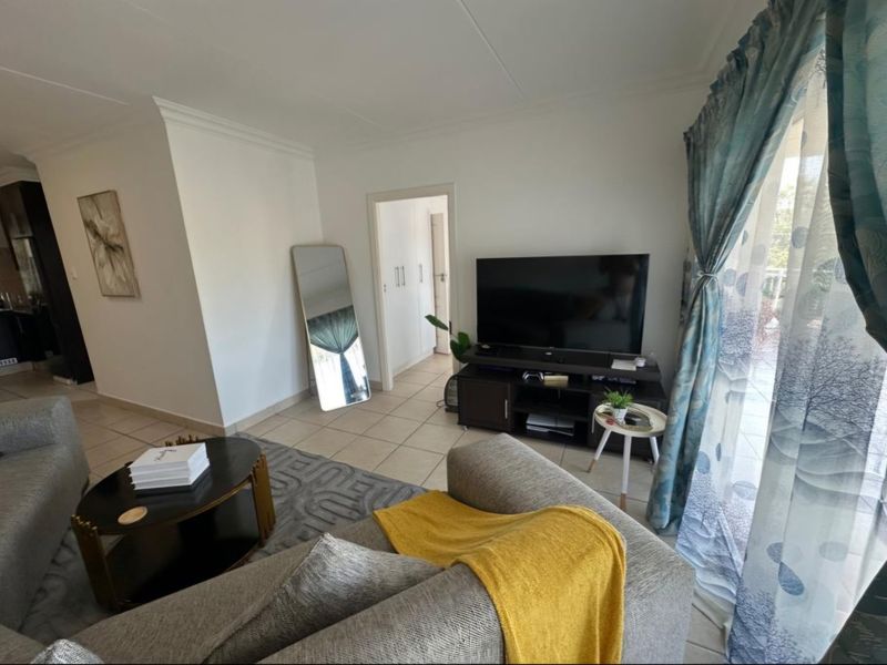 A bright living room featuring neutral tiled flooring, built-in storage cupboards, and a sliding door providing access to the outdoor area.