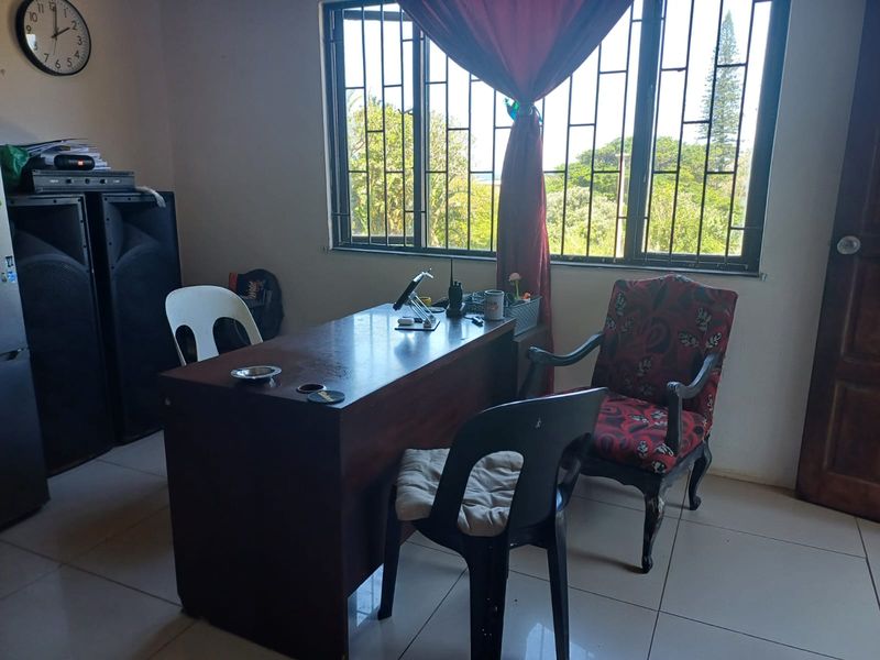 A functional home office space featuring tiled flooring and large windows fitted with security bars, offering natural light and garden views.