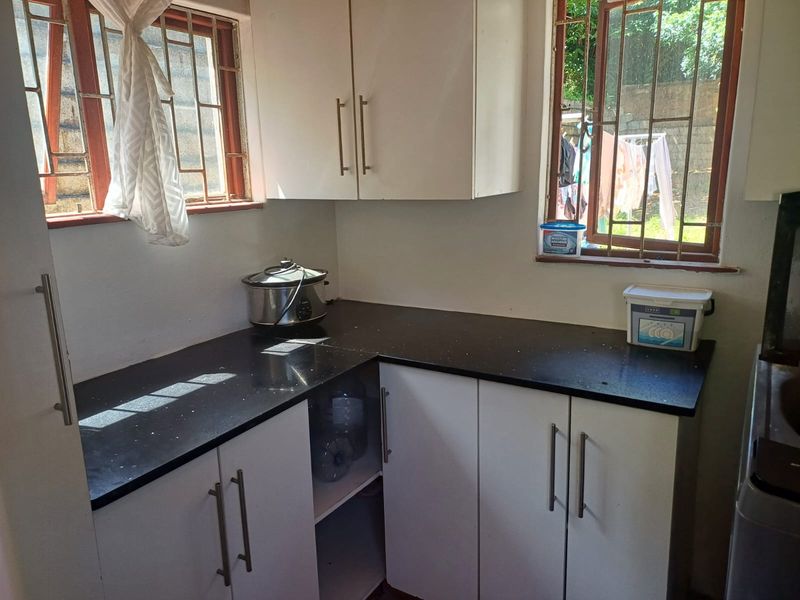 A functional kitchen area featuring white built-in cabinetry, dark laminate countertops, and windows fitted with security bars.