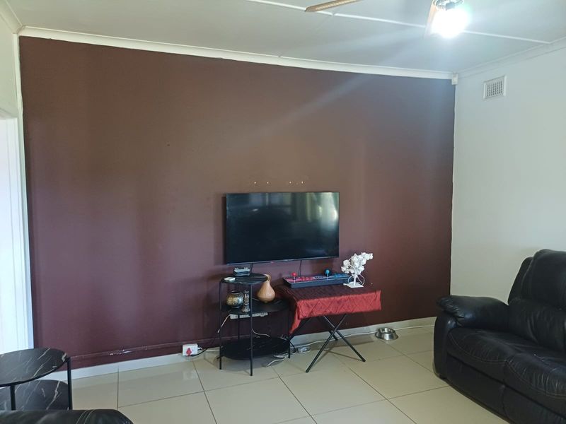 A living room featuring tiled flooring, a ceiling fan, and a dark accent wall with visible mounting points.